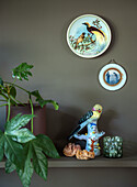 Shelf with porcelain bird figurine, decorative wall plates and potted plant