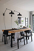 Simple dining room with wooden table, black chairs and wall lamps