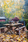 Herbstlicher Terrassentisch und Outdoor-Kamin umgeben von Laub