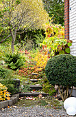 Gartenweg durch herbstlichen Gartenbereich neben Backsteinhaus