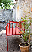 Red metal garden bench next to marigold plant in courtyard