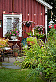 Idyllic garden corner in front of a red house wall with flowering plants and fairy lights