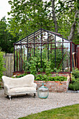 Garten mit Gewächshaus und Stein-Sofa vor Hochbeet aus Ziegelsteinen