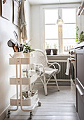 Light-coloured kitchen area with white rattan armchair and serving trolley