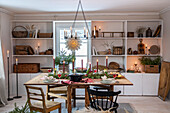 Christmas dining table with candles and fir branches in front of white shelves