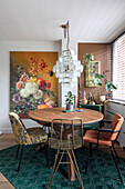 Dining room with round wooden table, assorted chairs, green carpet and large flower painting on the wall