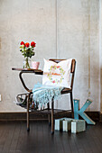 Decorative chair with bouquet of flowers, embroidered cushion and blanket in front of concrete wall