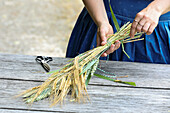 Frau bindet Strauß aus Gersten- und grünen Weizenähren