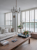 Bright living room with wooden table, crystal chandelier and large shutters