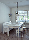 Dining area with white, rustic wooden table and bench in front of large windows