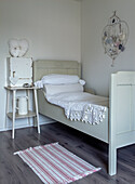 Child's bed with crocheted blanket, white side table and wall decoration