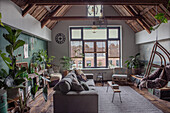 Living room with sloped beamed ceiling, lots of plants and rattan hanging chair