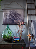 Wall decoration with nature picture, glass vase with plants and books on a chest