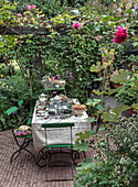 Laid garden table with tea service and cake under a rose arbour