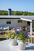 Sommerliche Blumendekoration mit Lupinen und Gänseblümchen auf weißem Terrassentisch