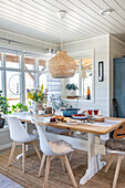 Dining room with richly laid table, white chairs and wicker lamp