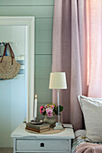 Bedside table in bedroom with bouquet of flowers, lit candle and table lamp