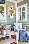 Cosy veranda with rustic wooden furniture, sage green wall and summer hat decoration