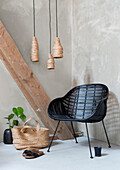 Black rattan armchair next to raffia bag and monstera plant, lights made from natural fibres