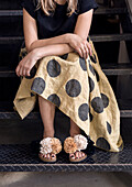 Person with polka dot skirt and sandals with pompoms on metal stairs