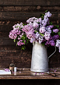 Lilacs (Syringa) in galvanized jug on rustic wooden table