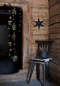 Rustic corner of a wooden hut with a garland of pine cones, twigs and golden acorns, black star on the wall