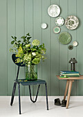 Bouquet of flowers in glass vase on dark green chair in front of green-painted wooden wall