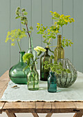 Glass vases with green and yellow flower arrangements on a rustic wooden table