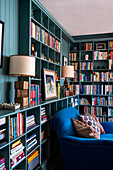 Green colored bookshelf wall with blue armchair