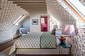 Bedroom in the attic with floral wallpaper and green-patterned throw on the bed