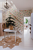 Entrance area with floral wallpaper, round wooden table and small fir tree