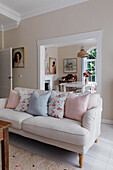 Bright living room with cream-coloured sofa and floral pattern cushions, view into the dining room