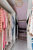 Dressing room with pink dotted wallpaper and clothes in the wardrobe