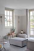 Bright living room with large windows, grey seating furniture and cat on pouf