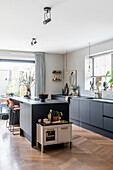 Modern kitchen with black island, herringbone parquet flooring and bar counter