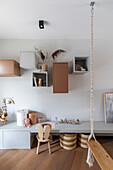 Modern children's room with swing, desk, wooden chair and wall shelves in earthy colours