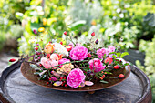 Flower arrangement with various roses (pink) and rose hips on a metal tray in the garden