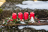 Adventsgesteck mit roten Kerzen und weihnachtlicher Dekoration im Schnee