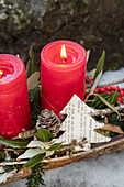 Red candles and pine cones with twigs and paper decorations on tree bark