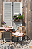 Rattan chair and table in front of wooden wall with decorative shutters and flower arrangement