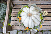 Weißer Kürbis verziert mit Herbstblumen auf Holzbank im Garten