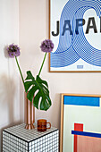 Monstera leaf and purple allium flowers in vase on tiled side table