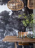 Wooden table with candles in front of photo wallpaper and glass vase with twigs