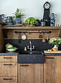 Rustic kitchen with wooden furniture and black stone sink, decorated with potted plants and crockery