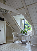 Sitting area in white-painted attic with wicker chairs and flower arrangement