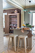 Kitchen island with bar stools and pendant lights, open cupboard with crockery in the background