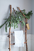 Decorative wooden ladder with fir branches and white towel