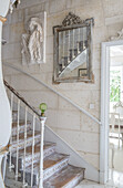 Staircase with antique sculpture and ornate mirror on stone wall