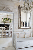 Entrance area with white wooden bench and chandelier, passageway to the dining room with floral arrangement