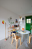 Brightly decorated room with round table, wooden chairs, shelf and green door